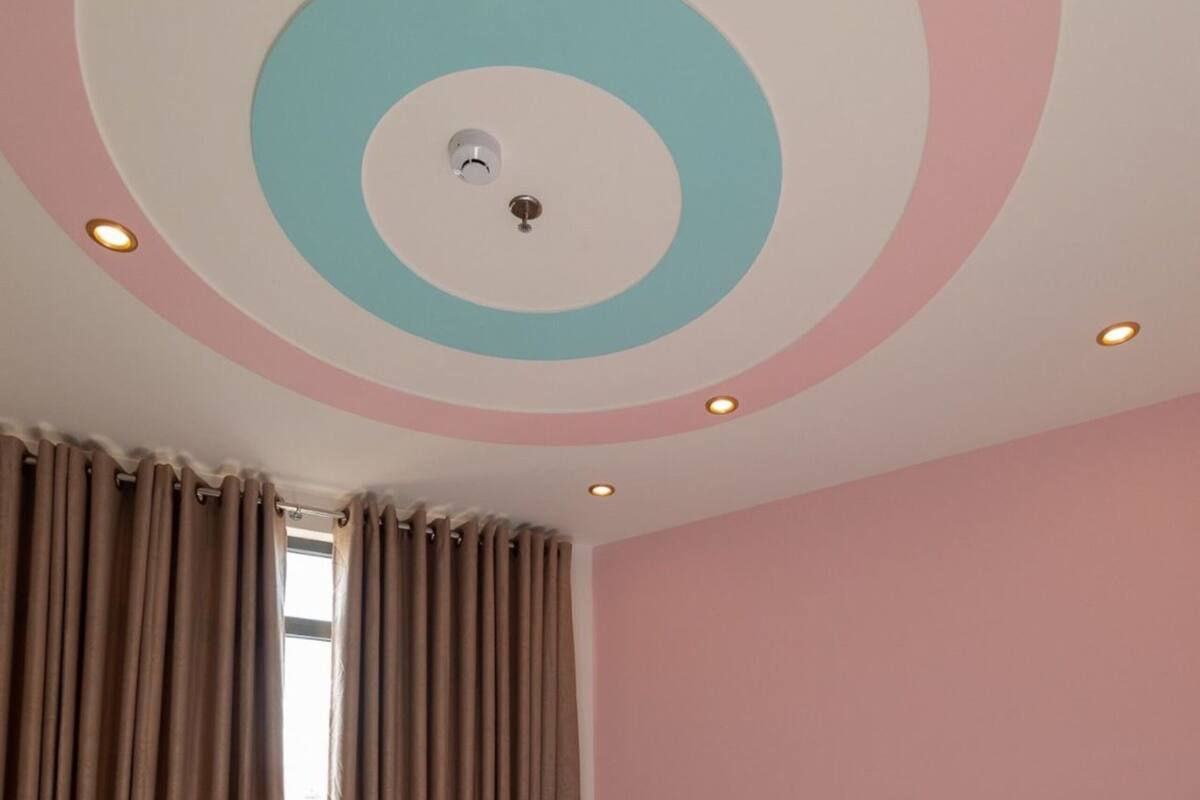 A bedroom with a bed, curtains, a teddy bear, and a ceiling with circular patterns.