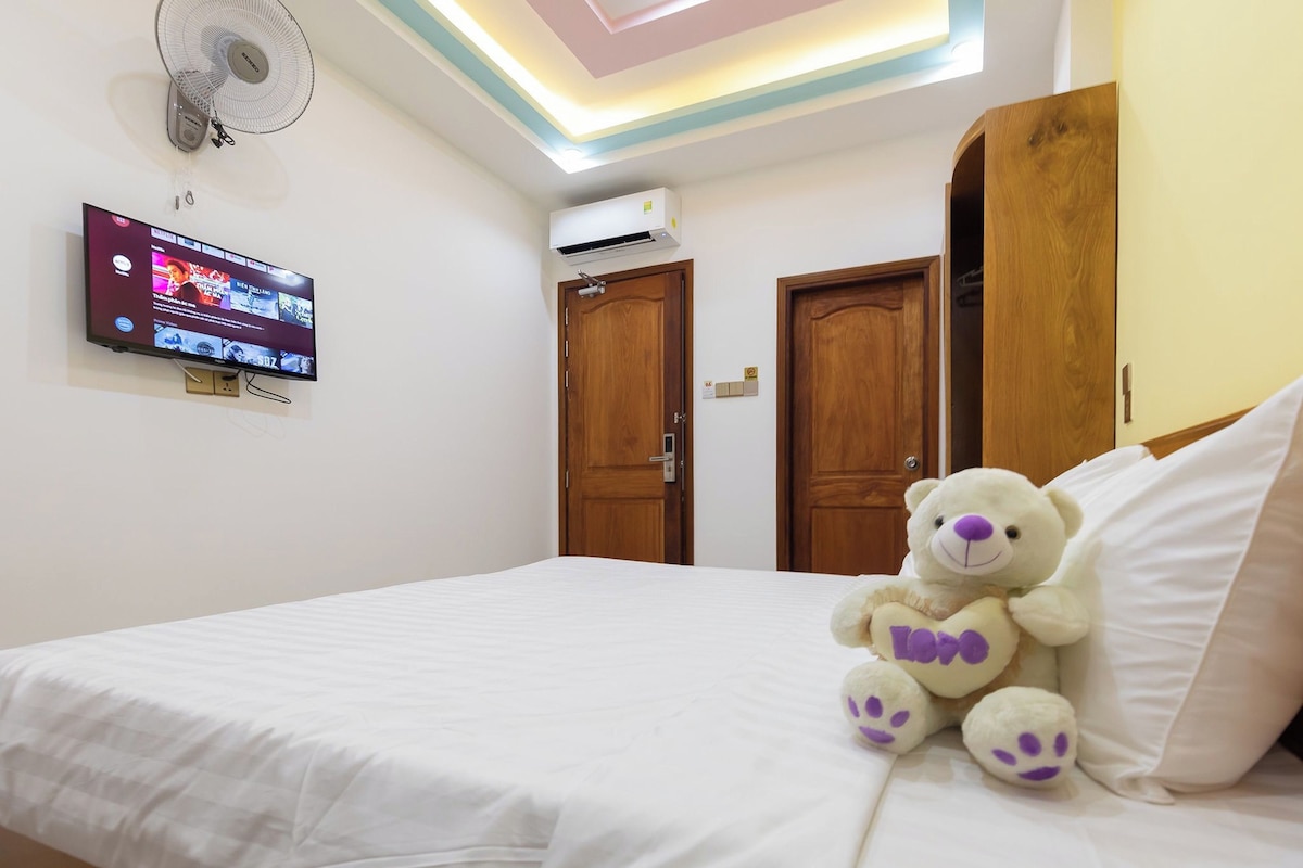 A bedroom with a bed, a television, an air conditioner, and a teddy bear.