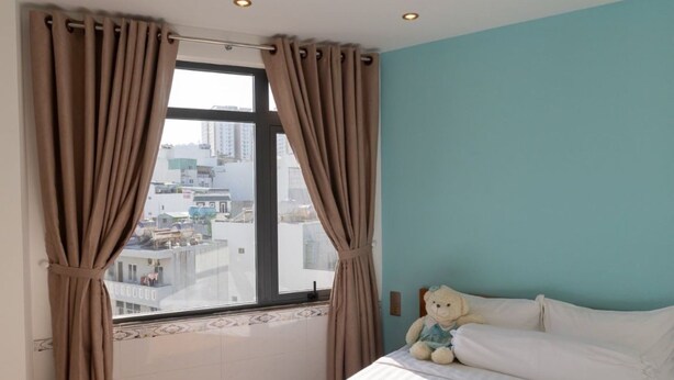 Een slaapkamer met een bed, een raam met gordijnen, uitzicht op gebouwen en een decoratief plafond.