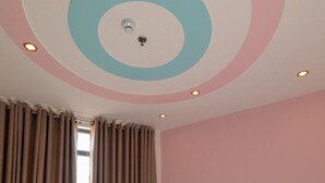 Een slaapkamer met een bed, gordijnen, een teddybeer en een plafond met cirkelmotieven.