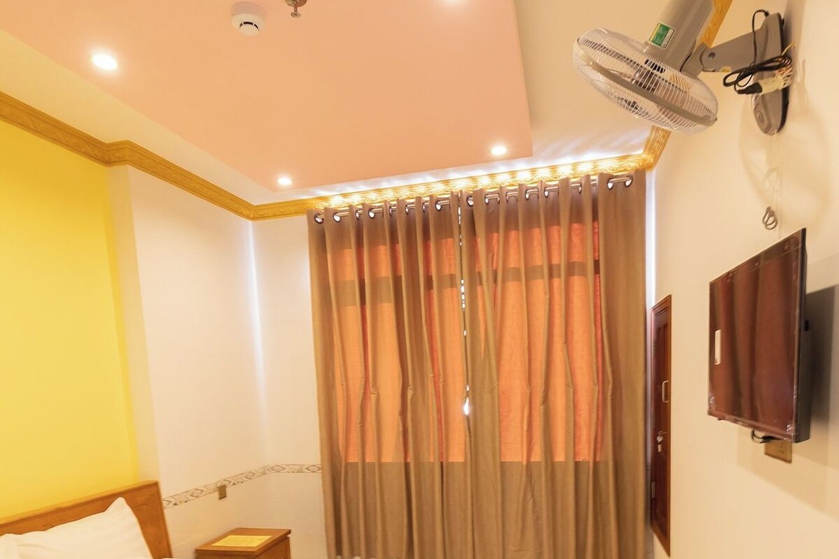 A hotel room with a bed, a bedside table, a wall-mounted TV, and a ceiling fan.