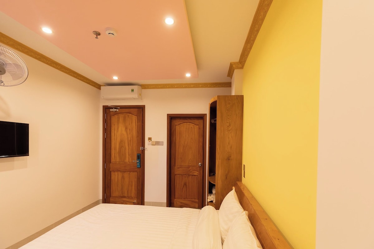 A bedroom with a bed, two wooden doors, a ceiling fan, and an air conditioning unit.