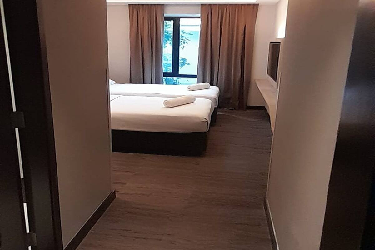 Un couloir d’hôtel menant à une chambre équipée d’un lit et d’une télévision.
