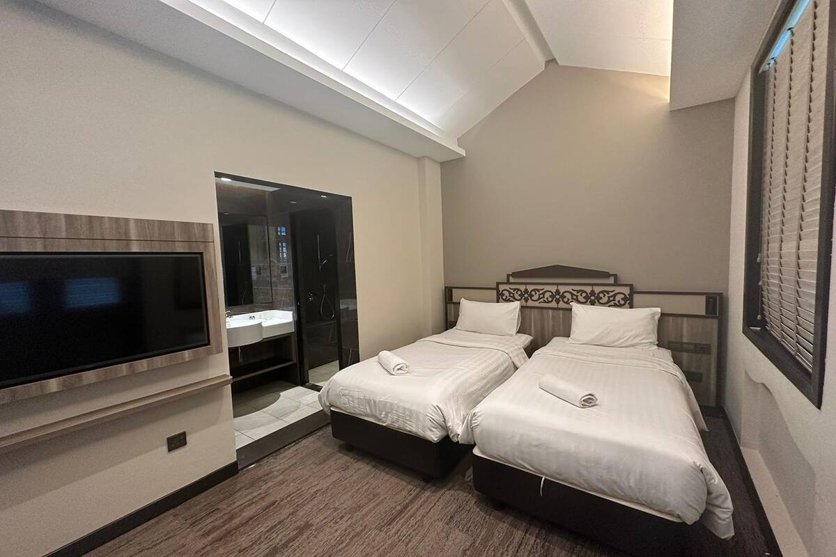 Une chambre d’hôtel avec deux lits, une télévision, une salle de bain avec douche et une grande fenêtre avec stores.