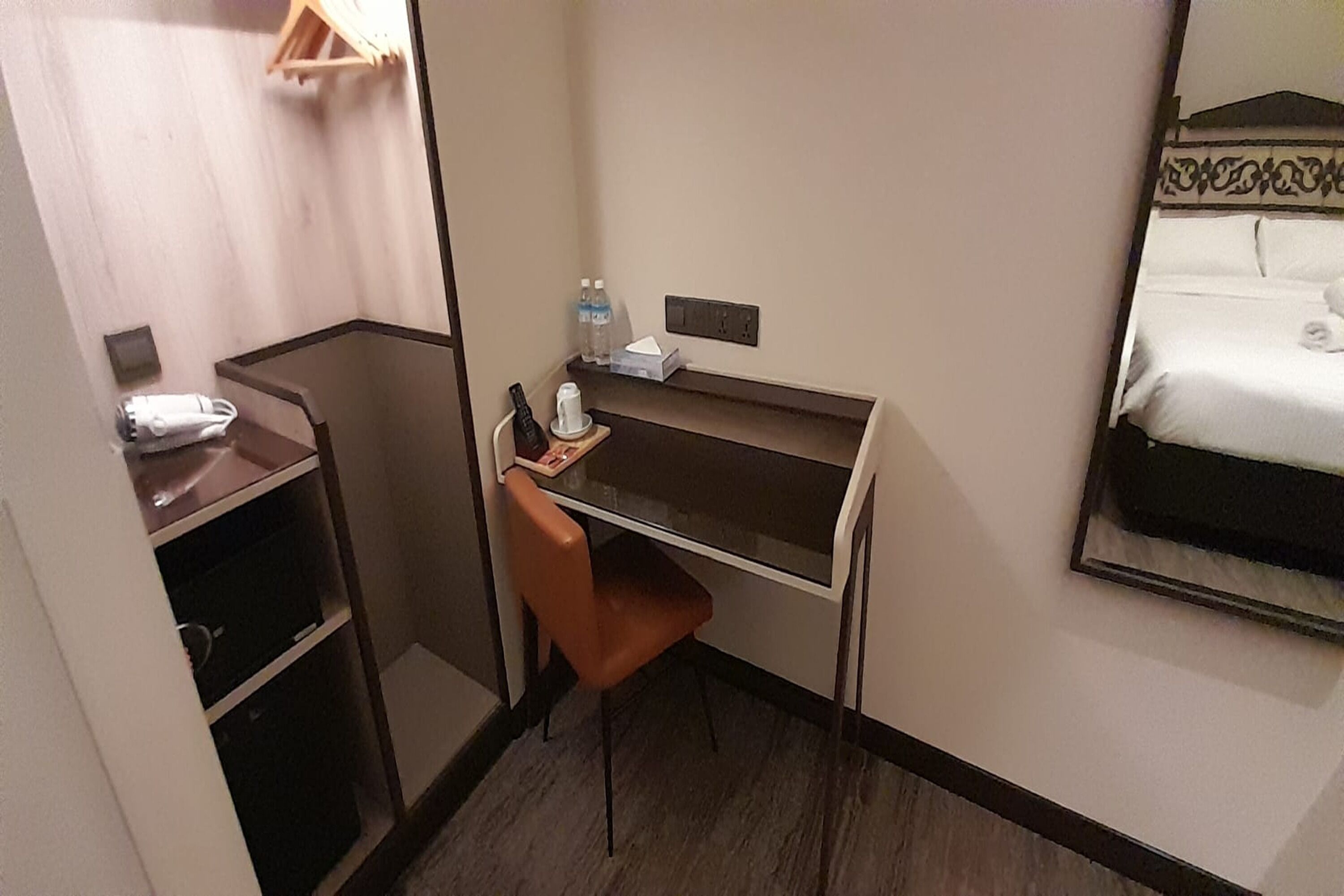 A compact hotel room with a desk, chair, and a bed. There are two bottles of water on the desk, a tissue box, and a remote control.