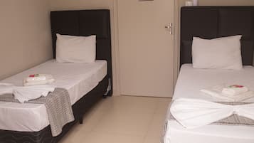 Two single beds with white linens and pillows, a door with a notice, and a tiled floor.