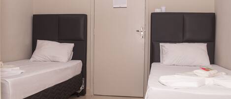 Two single beds with dark headboards and white bedding, a closed door with a notice, and a tiled floor.