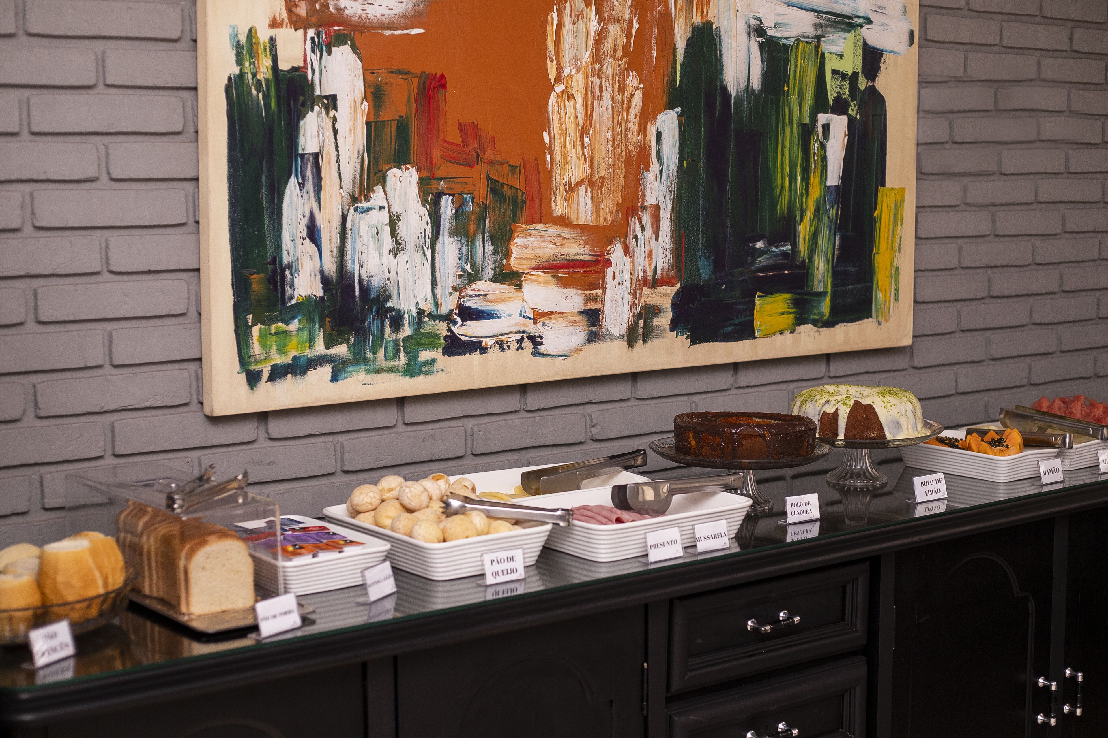 A buffet with various food items and a large abstract painting on the wall.