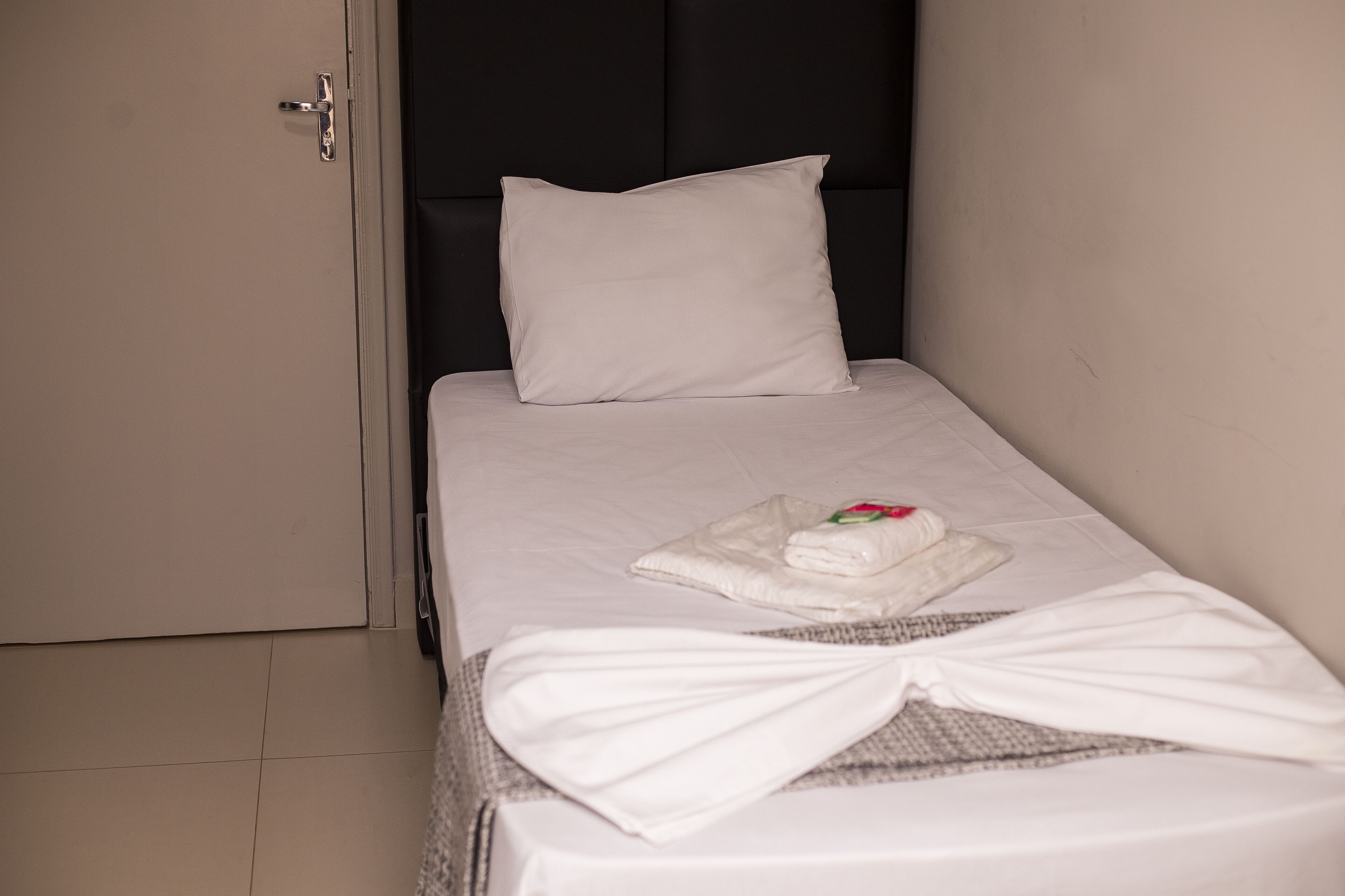 A small, neatly made bed with a white pillow and a folded towel on the bed.