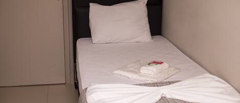 A small, neatly made bed with a white pillow and a folded towel on the bed.