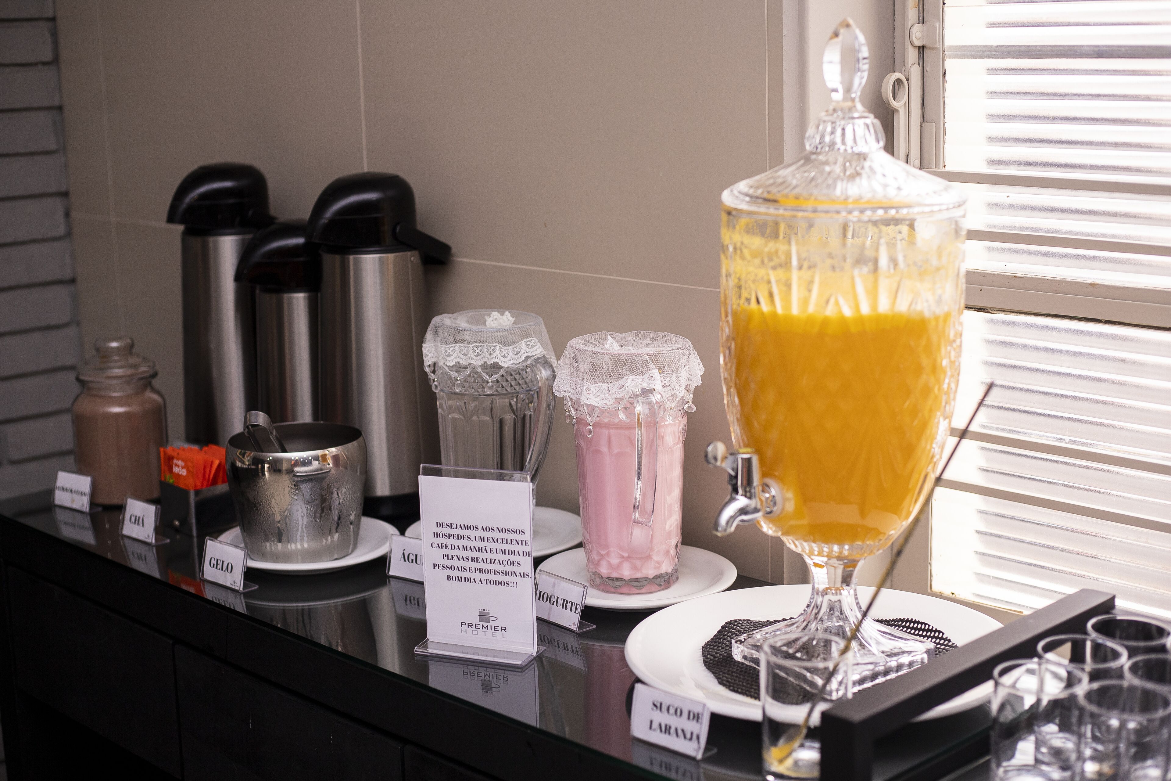 A breakfast bar with various food items and a large pitcher of orange juice.