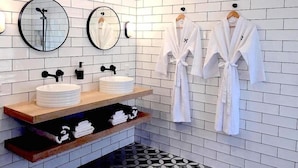 A modern bathroom with two sinks, a mirror, and two white robes hanging on hooks. - Motu Beachfront Art Villas (Rarotonga)