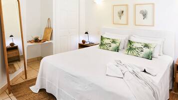 Een keurig opgemaakt slaapkamer met een groot bed, een nachtkastje met een lamp, een spiegel en twee ingelijste botanische prints aan de muur.