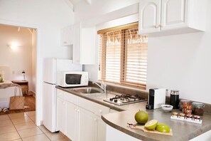 A kitchen with white cabinets, a microwave, a gas stove, and a window with blinds. - Motu Beachfront Art Villas (Rarotonga)