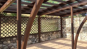 A wooden pergola structure with a stone wall and lattice fence in the background. - Casa il Cielo (Polpenazze del Garda)