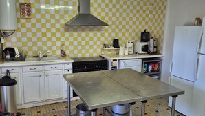 A kitchen with a checkered yellow and white backsplash, stainless steel appliances, and a metal table. - Group Lodging and Event Space: La Ferme d'Odette (Poucharramet)
