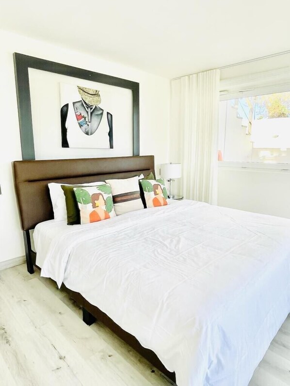 Una cama bien tendida con sábanas blancas, un cabecero de madera oscura y varios almohadones decorativos.