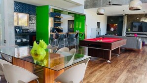 A modern living room with a glass dining table, pool table, and bar area with a green accent wall. - V12 Casa Summerhill  · Luxury villa w/ 2-level pool + bar and pool table (Sosúa)