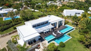 A modern house with a large swimming pool, surrounded by lush greenery and other houses. - V12 Casa Summerhill  · Luxury villa w/ 2-level pool + bar and pool table (Sosúa)