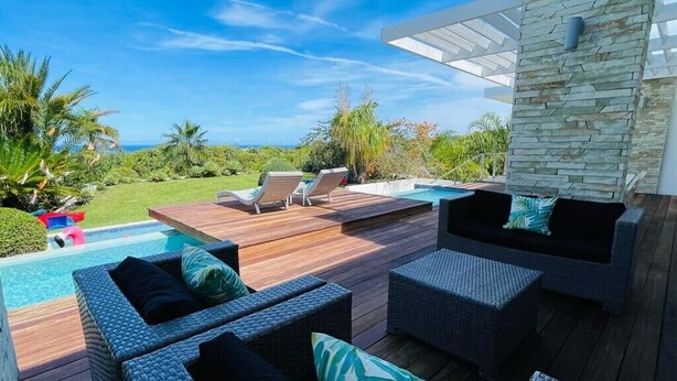 A poolside area with wicker furniture, a stone wall, and a view of the ocean. - V12 Casa Summerhill  · Luxury villa w/ 2-level pool + bar and pool table (Sosúa)