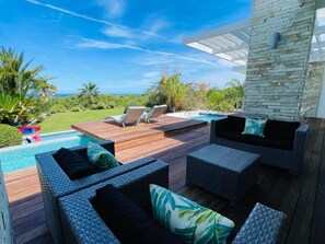 A poolside area with wicker furniture, a stone wall, and a view of the ocean.