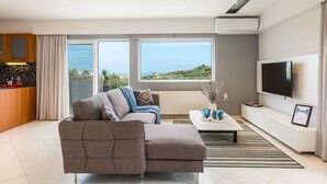 Ein modernes Wohnzimmer mit einer Couch, einem Couchtisch, einem Fernseher und Blick ins Freie.