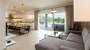 Ein modernes Wohnzimmer mit grauem Sofa, einem Essbereich mit Holztisch und Stühlen sowie einer Küche mit Pendelleuchten.