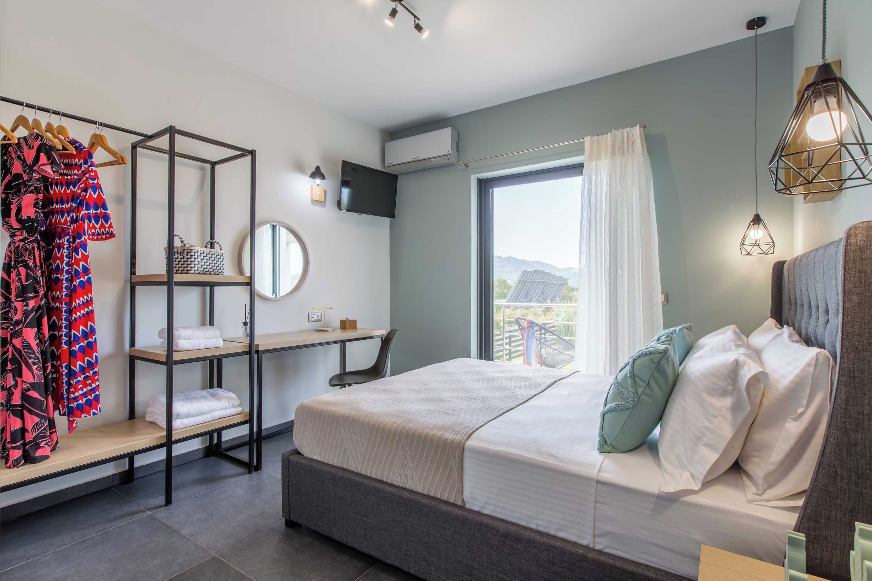 A modern bedroom with a bed, a desk, a chair, a wardrobe, and a large window.