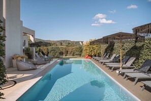 A swimming pool with lounge chairs and umbrellas, surrounded by greenery and hills in the background. - Villa Vega Heated* pool, next to nature! (Chania)
