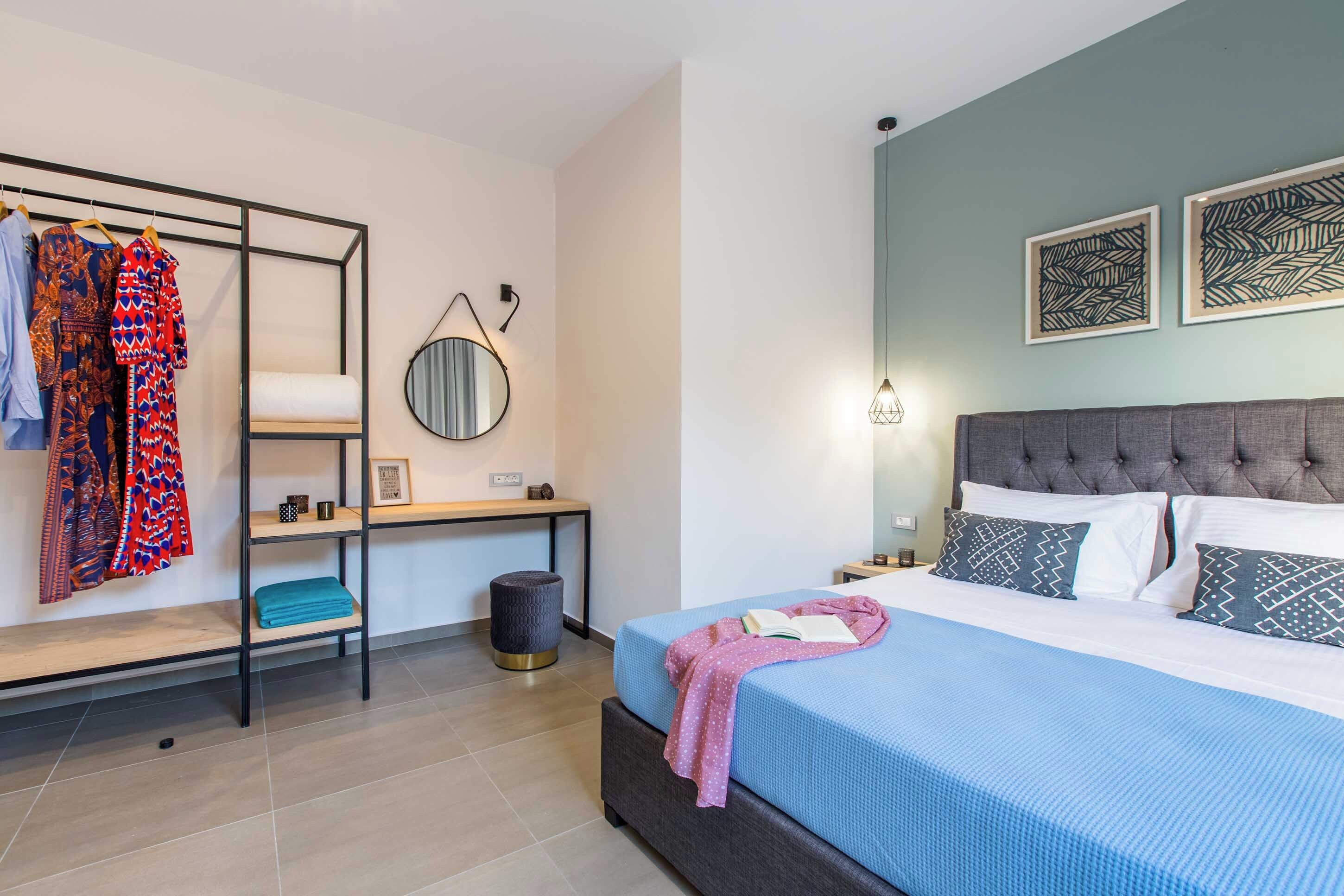 A bedroom with a bed, a bedside table, a wardrobe, a round mirror, and artwork on the wall.