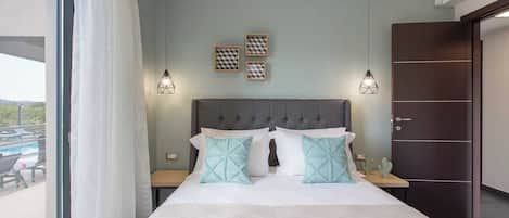Een slaapkamer met een groot bed, twee nachtkastjes, een grijs bekleed hoofdeinde en uitzicht op het landschap.
