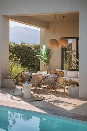 A poolside area with a seating arrangement, a table, and a hanging light fixture. - Villa Vega Heated* pool, next to nature! (Chania)