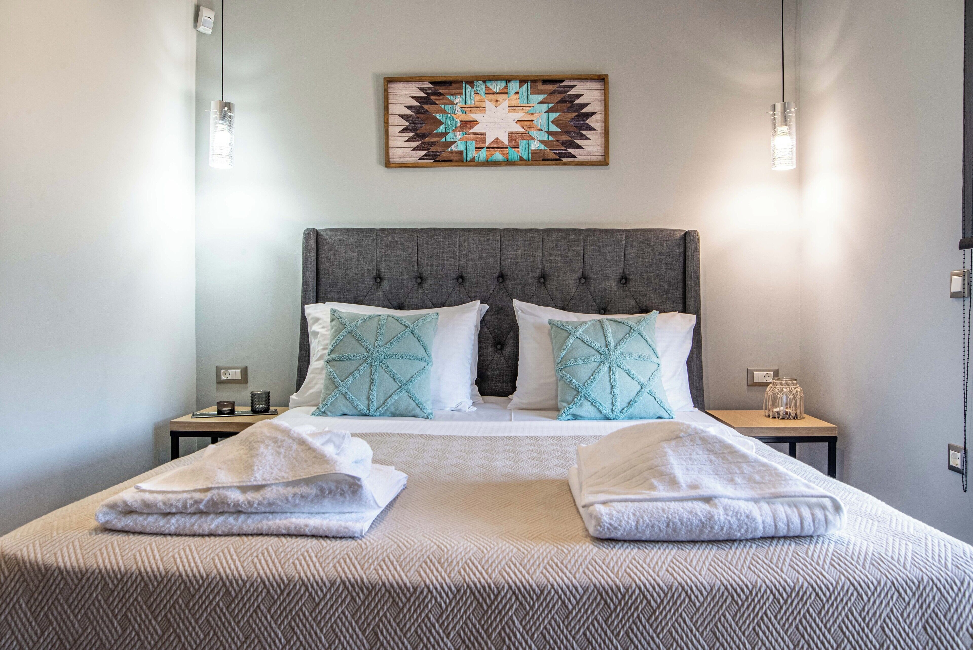 A neatly made bed with a grey upholstered headboard, two white pillows, and two matching throw blankets.