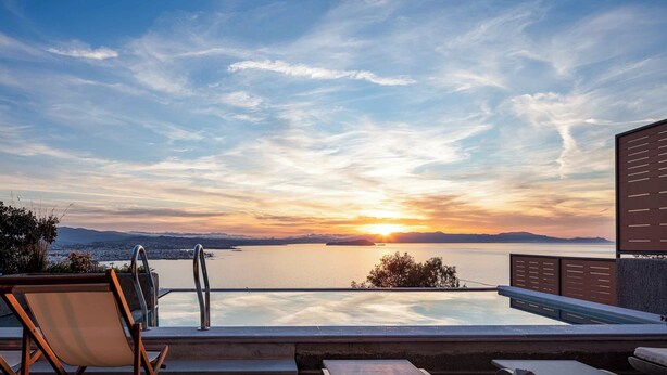 A poolside view with a sunset over water, lounge chairs, and a distant cityscape. - Omnia Villa l - Heated* pool & stunning Seaview! (Chania)