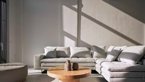 A modern living room with a sectional sofa, a round wooden coffee table, and a marble floor. - Omnia Villa l - Heated* pool & stunning Seaview! (Chania)