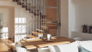 A modern interior with a wooden dining table, white chairs, a sofa with a blue pillow, and a staircase with wooden railings. - Omnia Villa II - Heated* pool & dazzling seaview! (Chania)