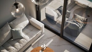 A modern living room with a sofa, a round wooden coffee table with a vase of flowers, and a large window offering a view of outdoor seating. - Omnia Villa II - Heated* pool & dazzling seaview! (Chania)