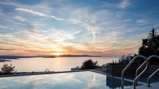 A swimming pool with a view of the sunset over a body of water, surrounded by greenery and a clear sky. - Omnia Villa II - Heated* pool & dazzling seaview! (Chania)