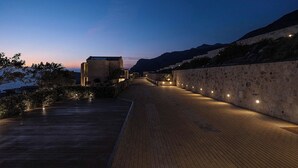 Un sendero pavimentado que conduce a un edificio, con un muro de piedra a un lado y una montaña al fondo.