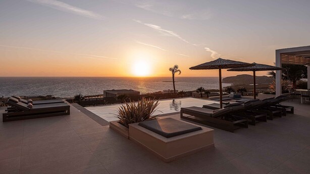 Zona de piscina en la azotea con tumbonas, una piscina pequeña y vista al océano al atardecer.