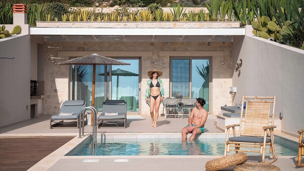 Un área de piscina moderna al aire libre con un muro de piedra, sillones de descanso y una mesa de comedor.