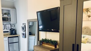 A modern bedroom with a large wardrobe, a television mounted above a wooden dresser, and a bed with a white duvet. - Perfectly Located Fully Remodeled Desert Casita (Bermuda Dunes)