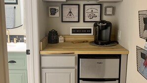 A compact kitchen with a microwave, coffee maker, and a refrigerator. There are framed motivational quotes on the wall and a small plant on the countertop. - Perfectly Located Fully Remodeled Desert Casita (Bermuda Dunes)