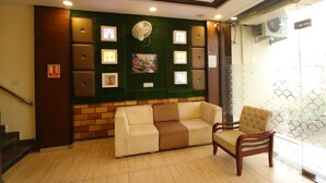 A lobby with a sofa and armchair, a wall-mounted fan, framed pictures, and a staircase. - Hotel Eurasia Mohali Airport (Mohali)