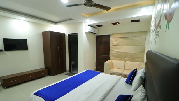 A bedroom with a bed, a ceiling fan, a TV, a wardrobe, and a sofa. - Hotel Eurasia Mohali Airport (Mohali)