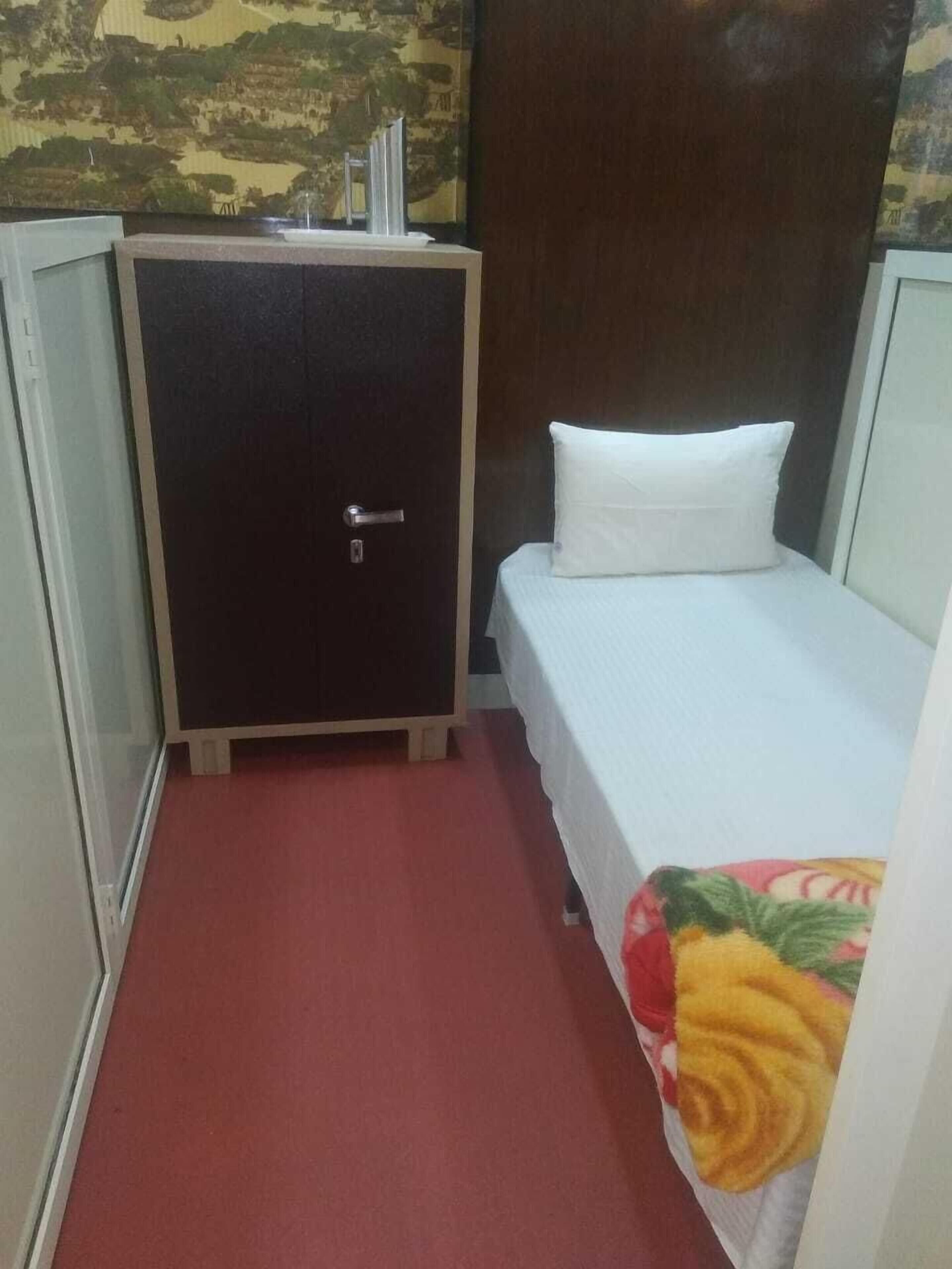 A small room with a bed, a nightstand, a wardrobe, and a red carpet.