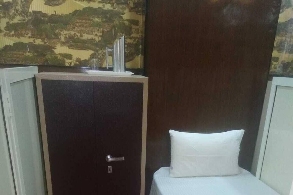 A small room with a bed, a nightstand, a wardrobe, and a red carpet.