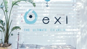 A sign with the word "exi" and the phrase "THE ULTIMATE EXPERIENCE" on a white background. - Exi Sea Side Suites (Santorini)