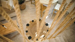 A view from a window overlooking a room with a woven floor mat, a wooden table, and a chair. - Exi Sea Side Suites (Santorini)