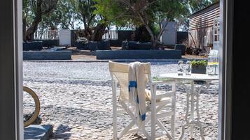 Vista a través de un ventanal a un patio con una silla blanca, una mesa y plantas en macetas.